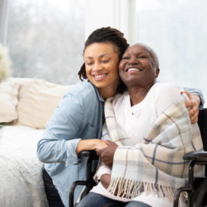 A daughter puts her arms around a smiling mother wrapped up in a blanket, sitting in a wheelchair.